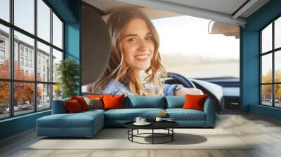 Close up portrait of pleasant looking female with glad positive expression, being satisfied with unforgettable journey by car, sits on driver`s seat, enjoys music. People, driving, transport concept Wall mural